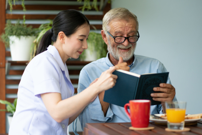 Young nurse and elderly man reading a bokk while smilling